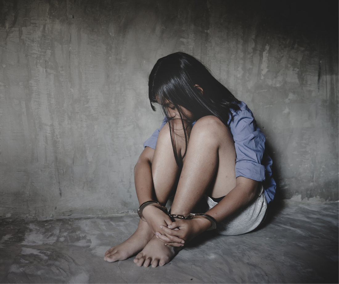 A young girl handcuffed and held prisoner, alone in a cell.